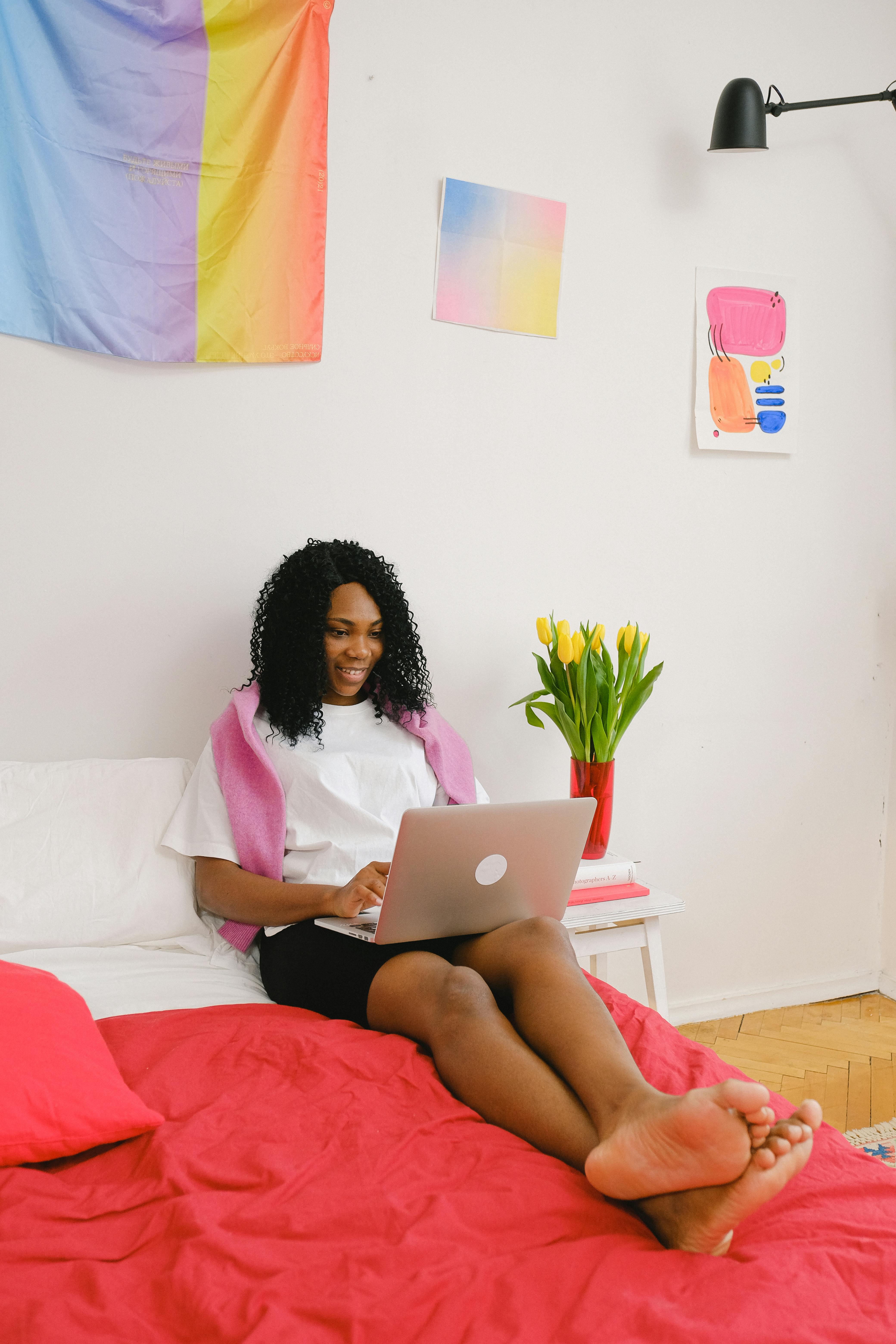 joyful black woman surfing laptop in bedroom