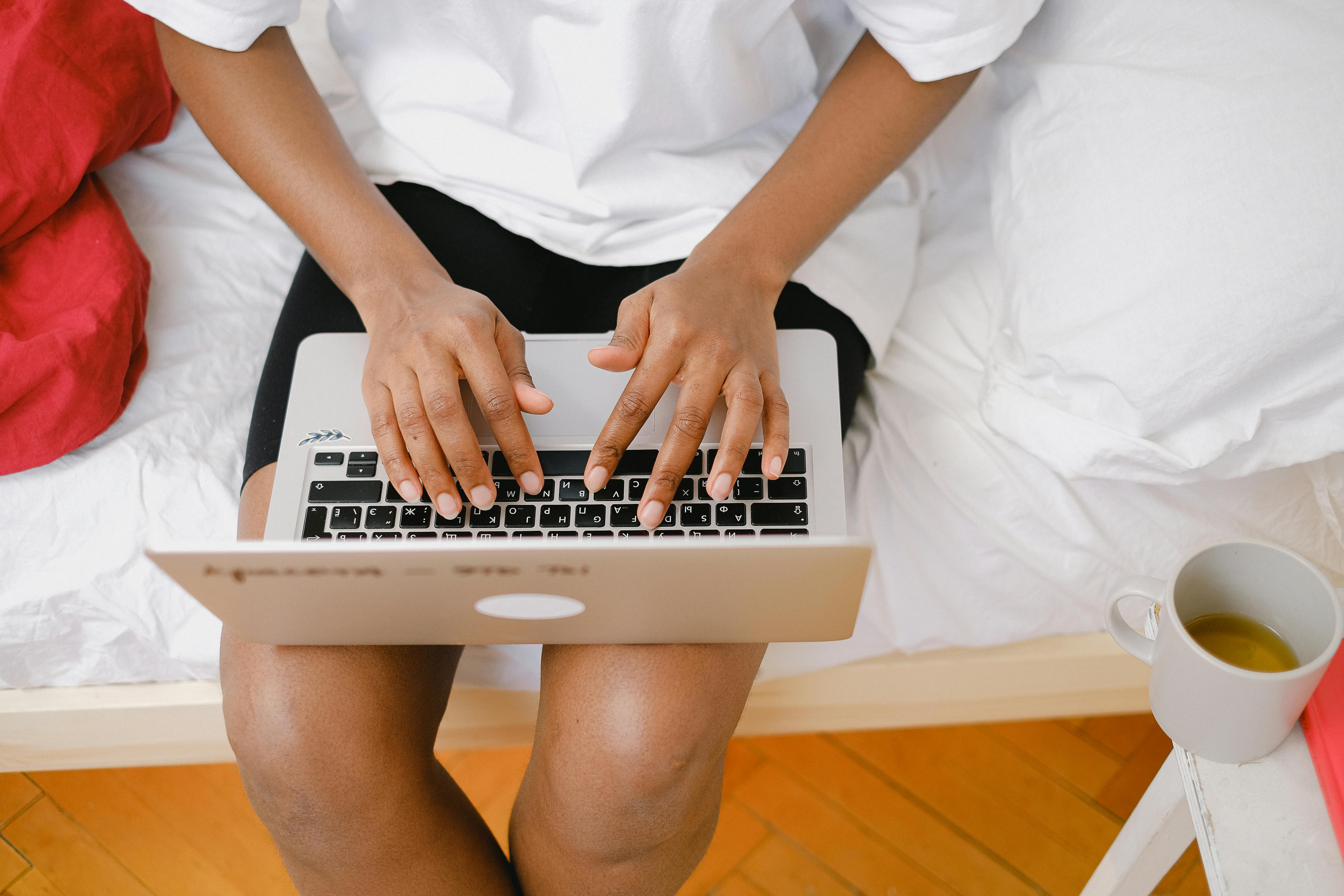 black woman typing on laptop near cup with tea