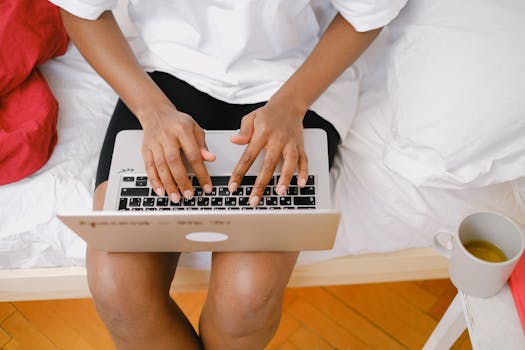 A woman works on her laptop from bed, enjoying a relaxed work-from-home atmosphere.