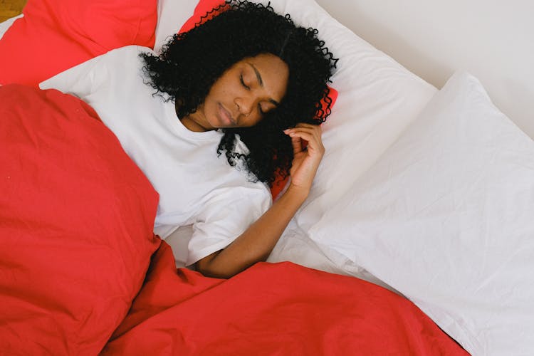 Relaxing Black Woman Lying On Soft Bed With Red Blanket