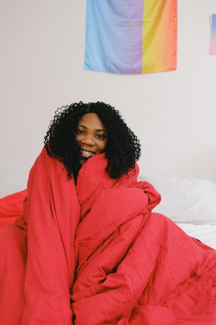 Cheerful young African American female in soft red blanket in modern bedroom in daylight