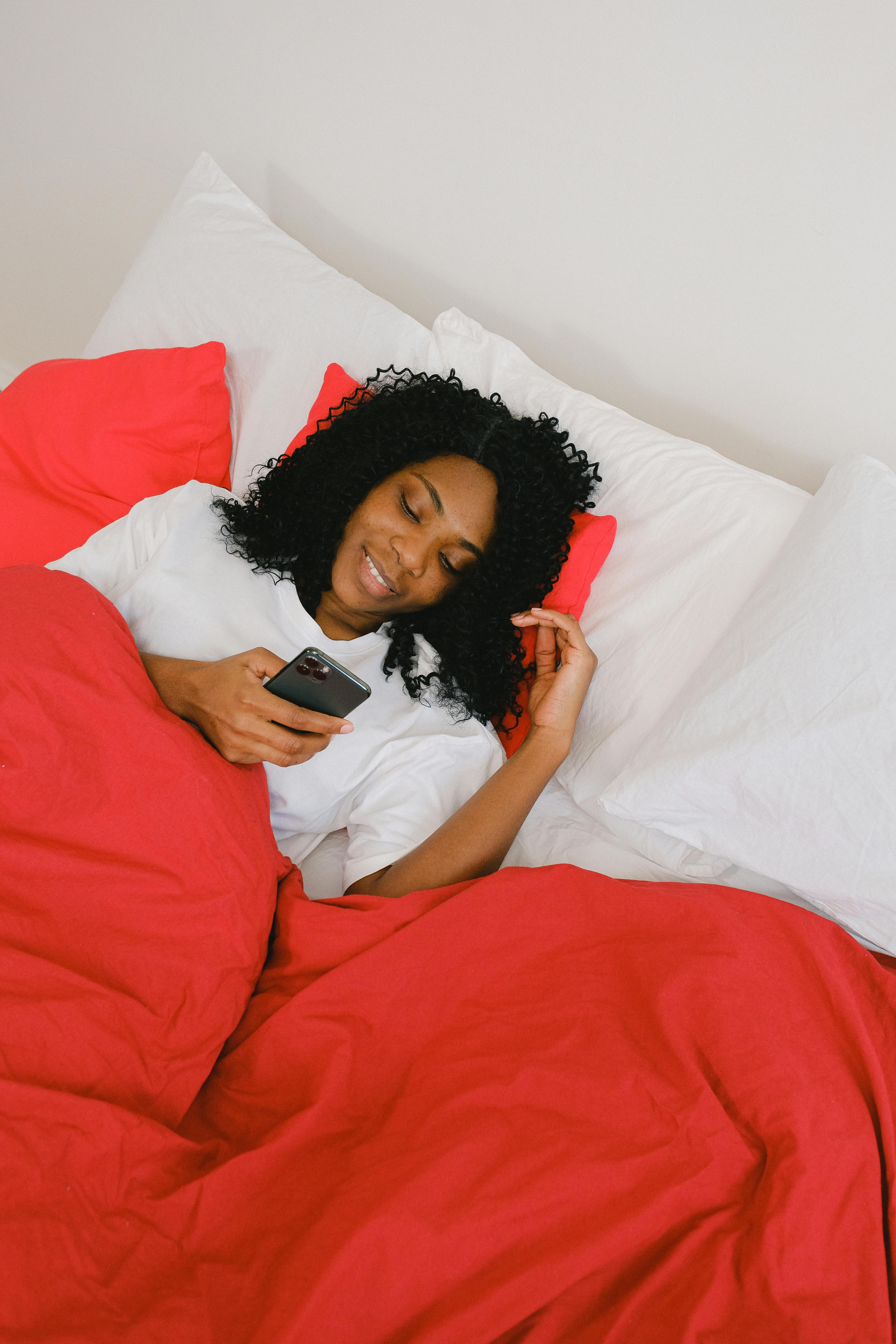 happy black woman using smartphone under red blanket