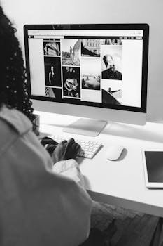 Black and white of crop anonymous African American female working with computer at table with tablet