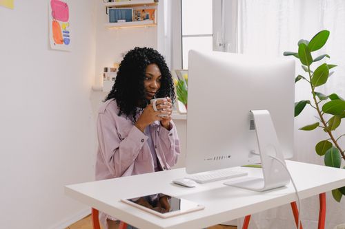 Free Positive African American female with cup of hot coffee using computer at table in daytime Stock Photo
