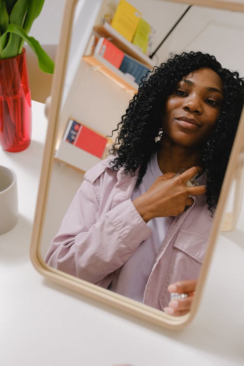 Free Black woman spreading perfume on neck while looking at mirror Stock Photo