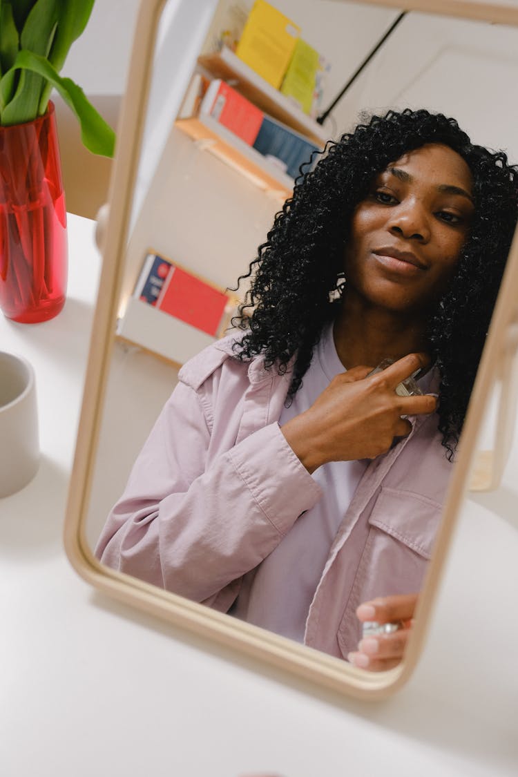 Black Woman Spreading Perfume On Neck While Looking At Mirror