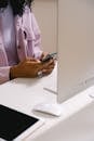 Crop unrecognizable African American female using mobile phone at white table with convenient computer in office