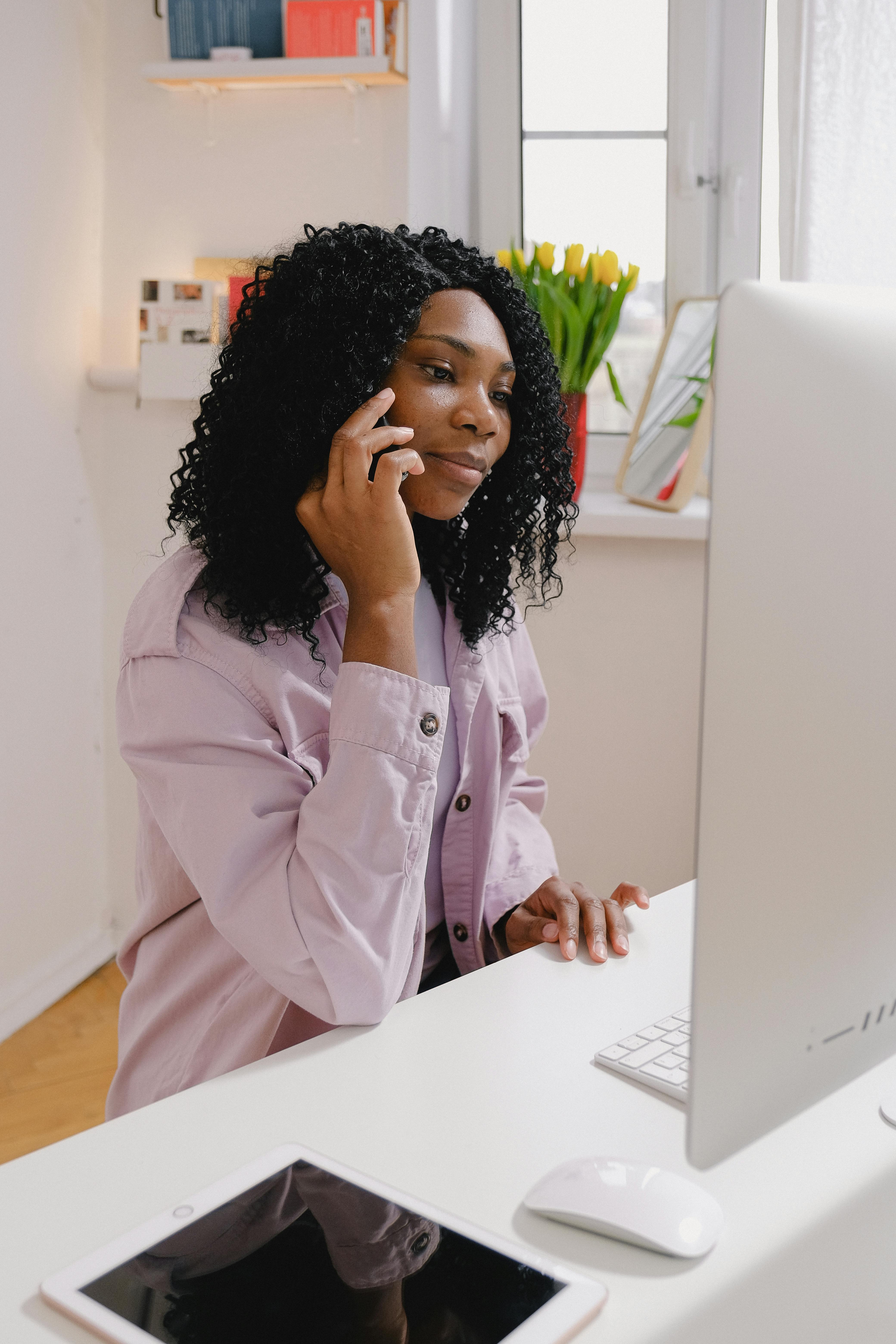 pleasant black freelancer talking on smartphone at table with computer