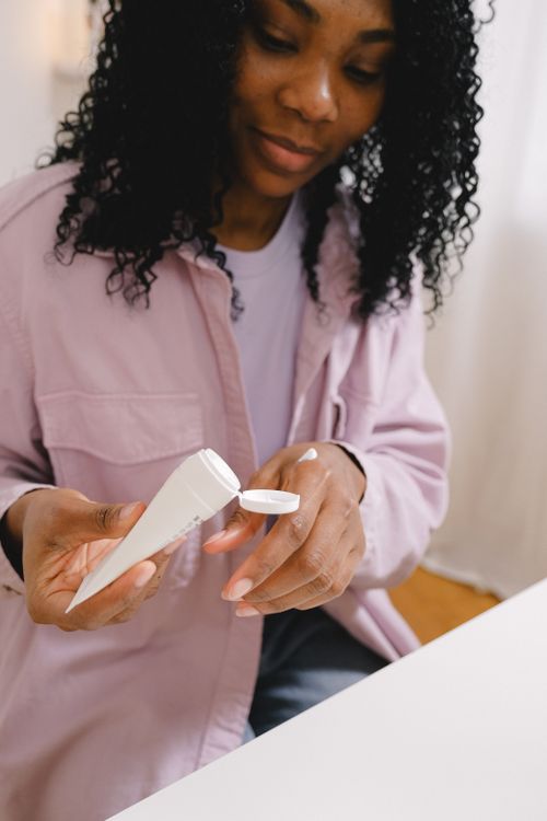 Free A woman with curly hair applying cream in a bright indoor setting. Ideal for skincare themes. Stock Photo