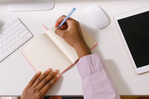 From above of crop unrecognizable African American employee writing in empty organizer at white table