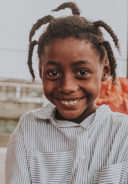 Free Portrait of a smiling child with braided hair outdoors, expressing joy and warmth. Stock Photo