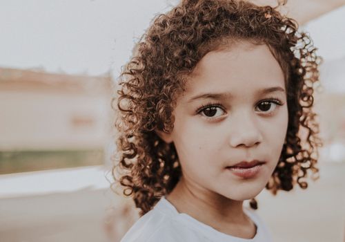 Free Charming close-up portrait of a young girl with curly hair captured outdoors. Warm and inviting. Stock Photo
