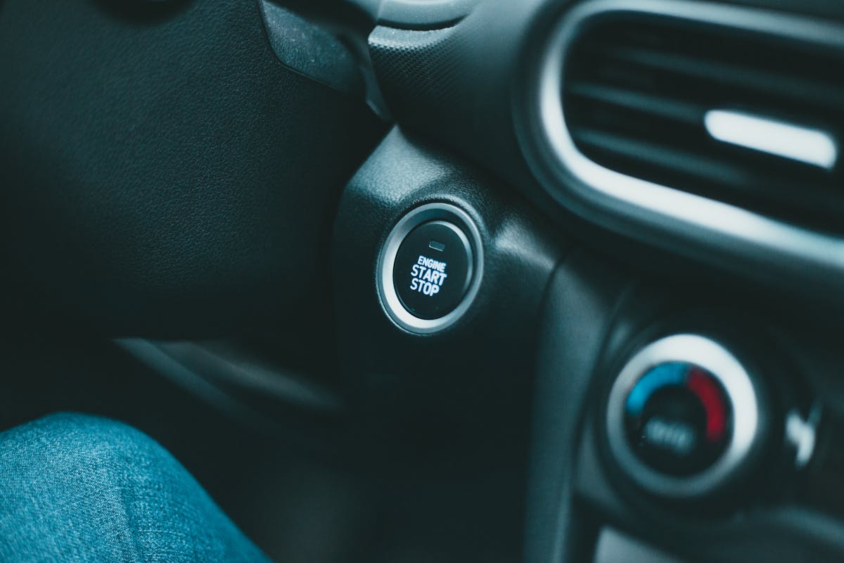 Closeup of black shiny dashboard with engine start button and conditioner controller of modern car in daylight