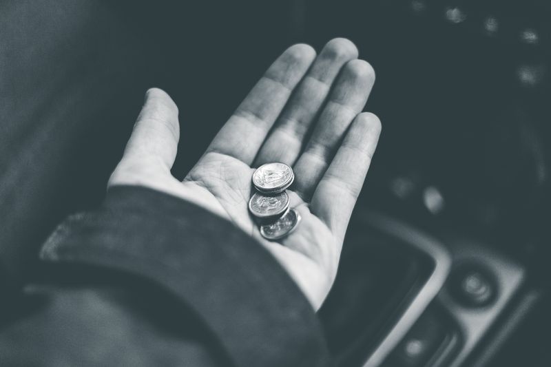 Black and white crop anonymous person demonstrating shiny coins while sitting in car on blurred background