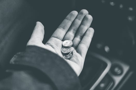 Close-up black and white photo of coins held in a person's hand inside a vehicle.