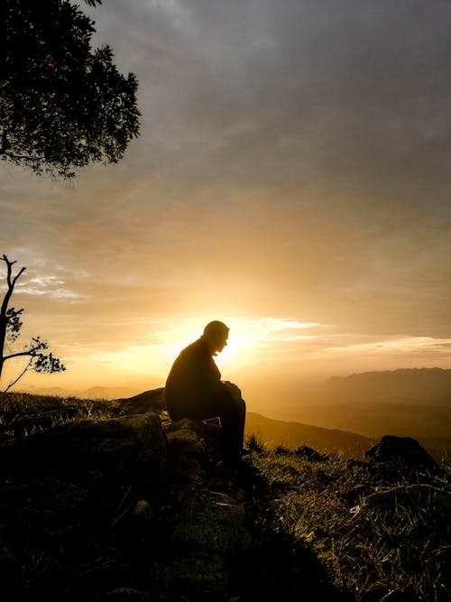 Silhouette of Man Sitting on the Stone During Sunrise