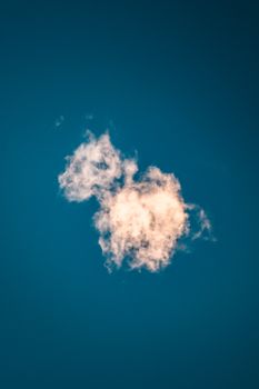 A singular fluffy cloud floating against a vibrant blue sky, captured in Italy.