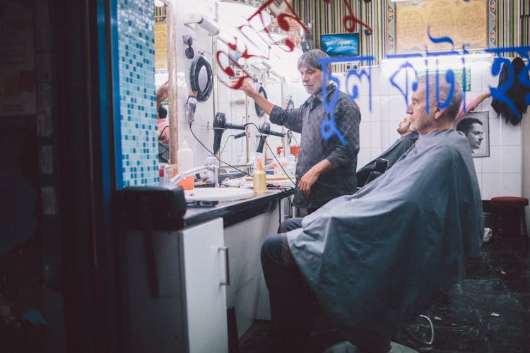 Elderly Man Sitting In The Chair With Blue Apron In Barbershop