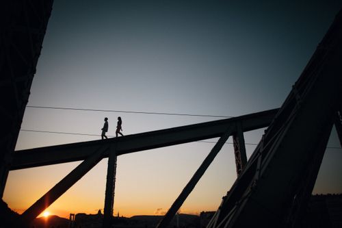 Free Two people walking on a bridge silhouetted against a vibrant sunset sky. Stock Photo