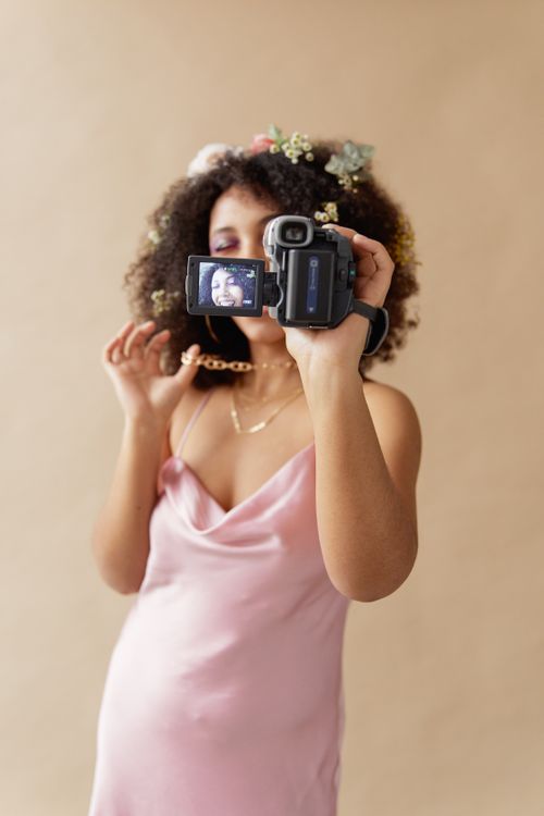 Free A woman with curly hair captures a video using a handheld camera. Stock Photo