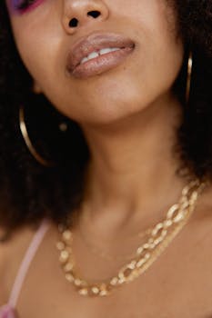 Close-up of a woman wearing bold gold necklaces and hoop earrings, showcasing modern fashion.