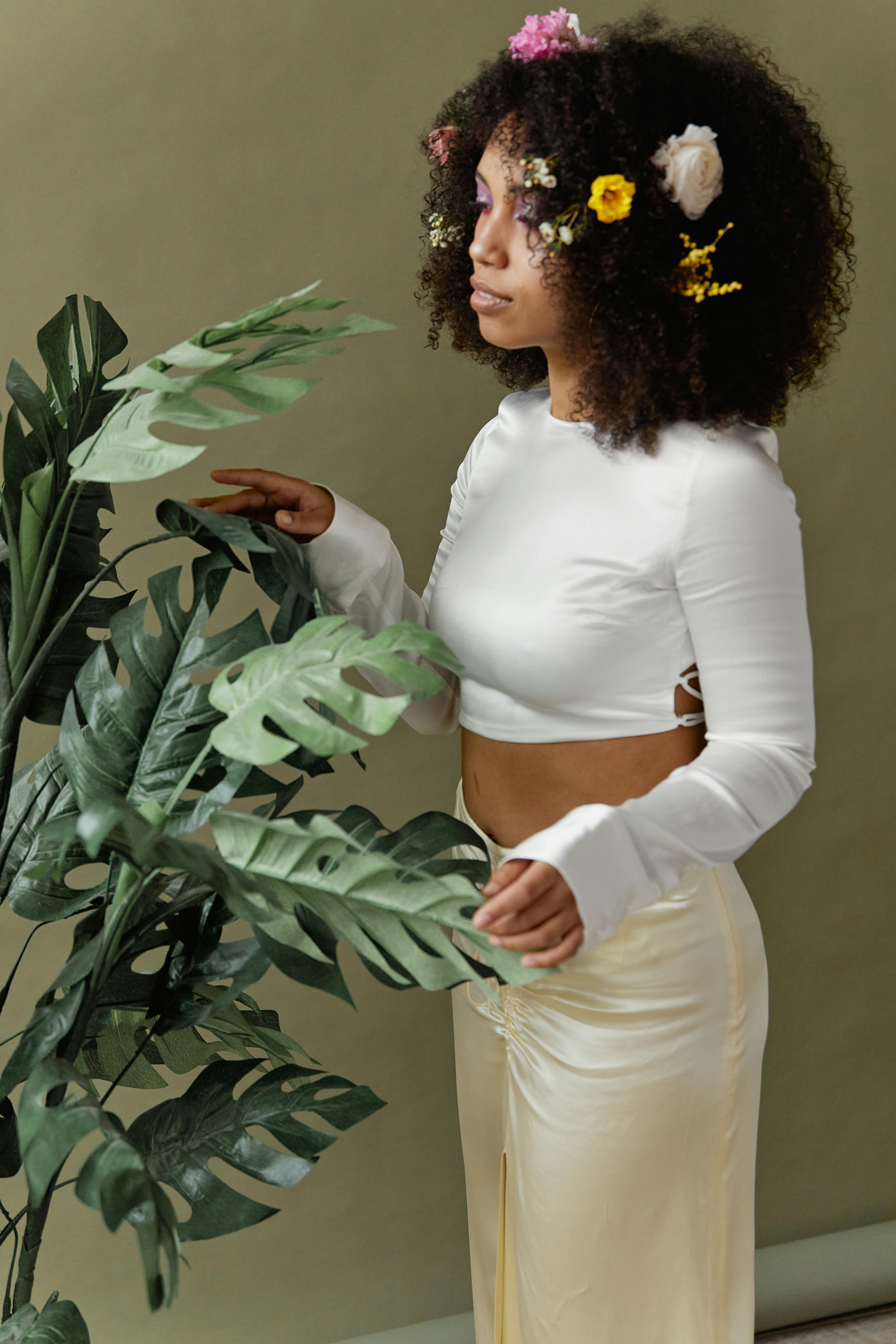 Young woman with floral hair accessories standing by a plant indoors.