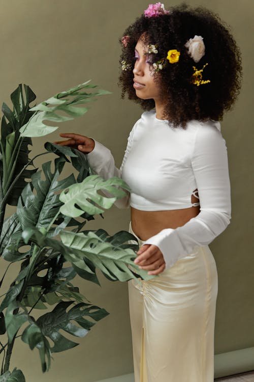 An Afro-Haired Woman in White Top Standing beside a Plant