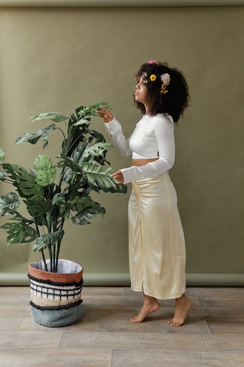Woman in White Long Sleeve Dress Touching Potted Green Plant