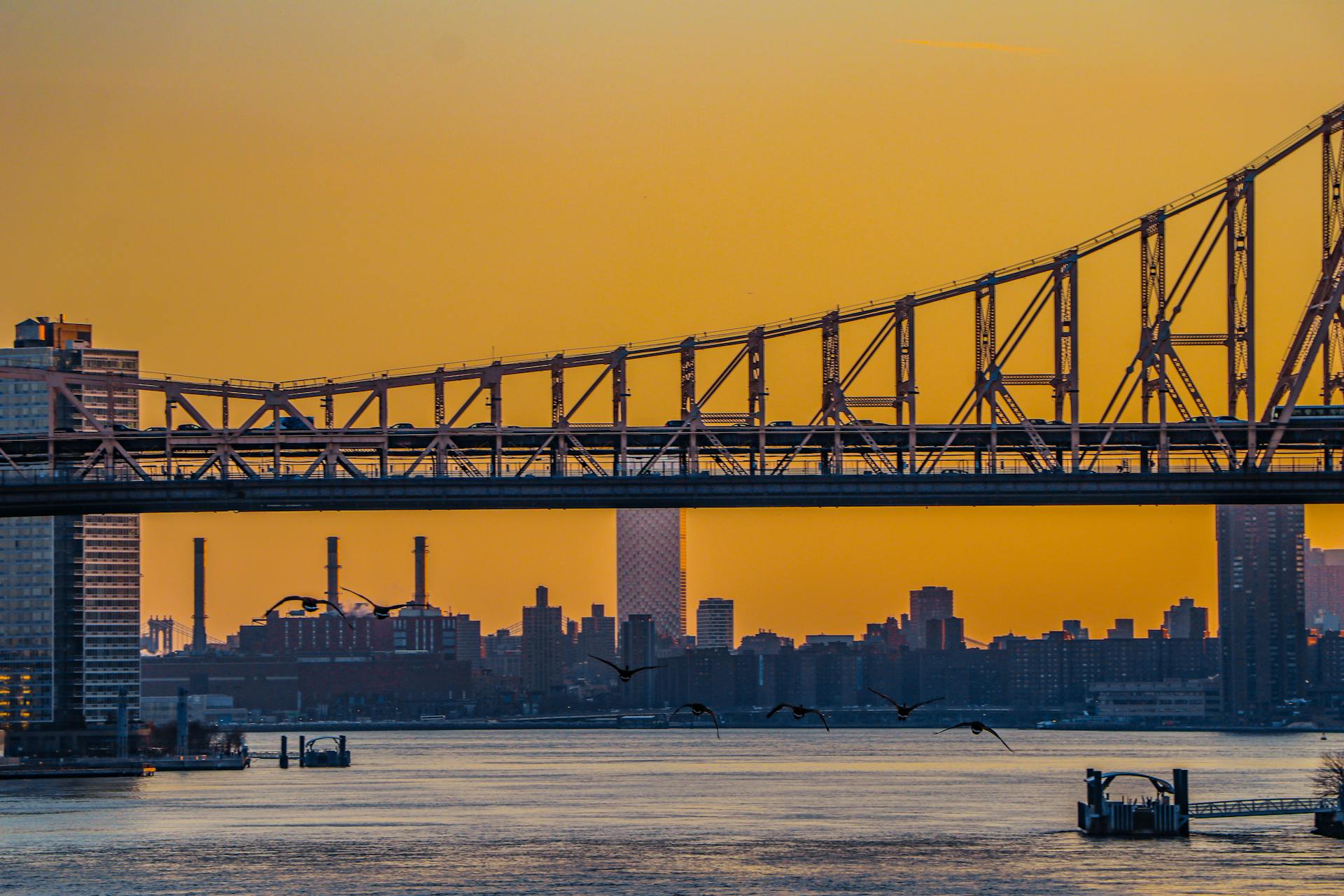 Capture of New York City's skyline at dusk featuring the iconic bridge against a warm, yellow sky.