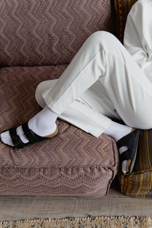 Free Person in White Pants and Black Slide Sandals Sitting on Sofa Stock Photo