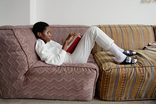 Woman in White Long Sleeve Shirt Sitting on Couch Reading a Book