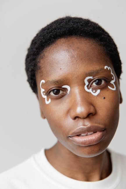 Artistic close-up portrait of a woman with unique white face paint on a neutral background.