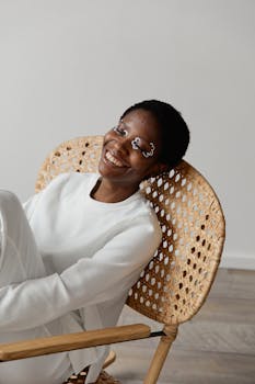 Cheerful woman with face paint sits in a wicker chair, wearing white clothing and smiling.