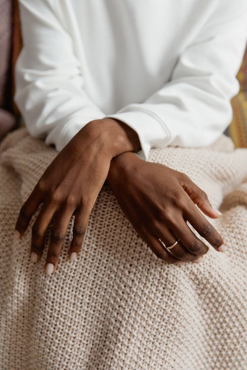 Free A close-up shot of hands with nail polish and a ring resting on a knitted blanket. Stock Photo