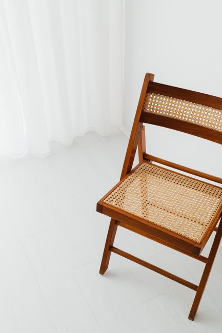 Elegant wooden folding chair against white curtains and walls, showcasing minimalist design.