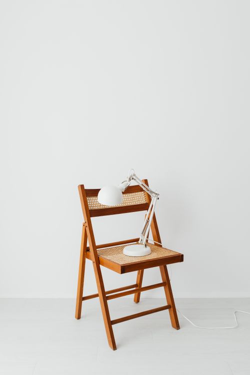 Free Sleek wooden folding chair with a white desk lamp against a minimalist background. Stock Photo