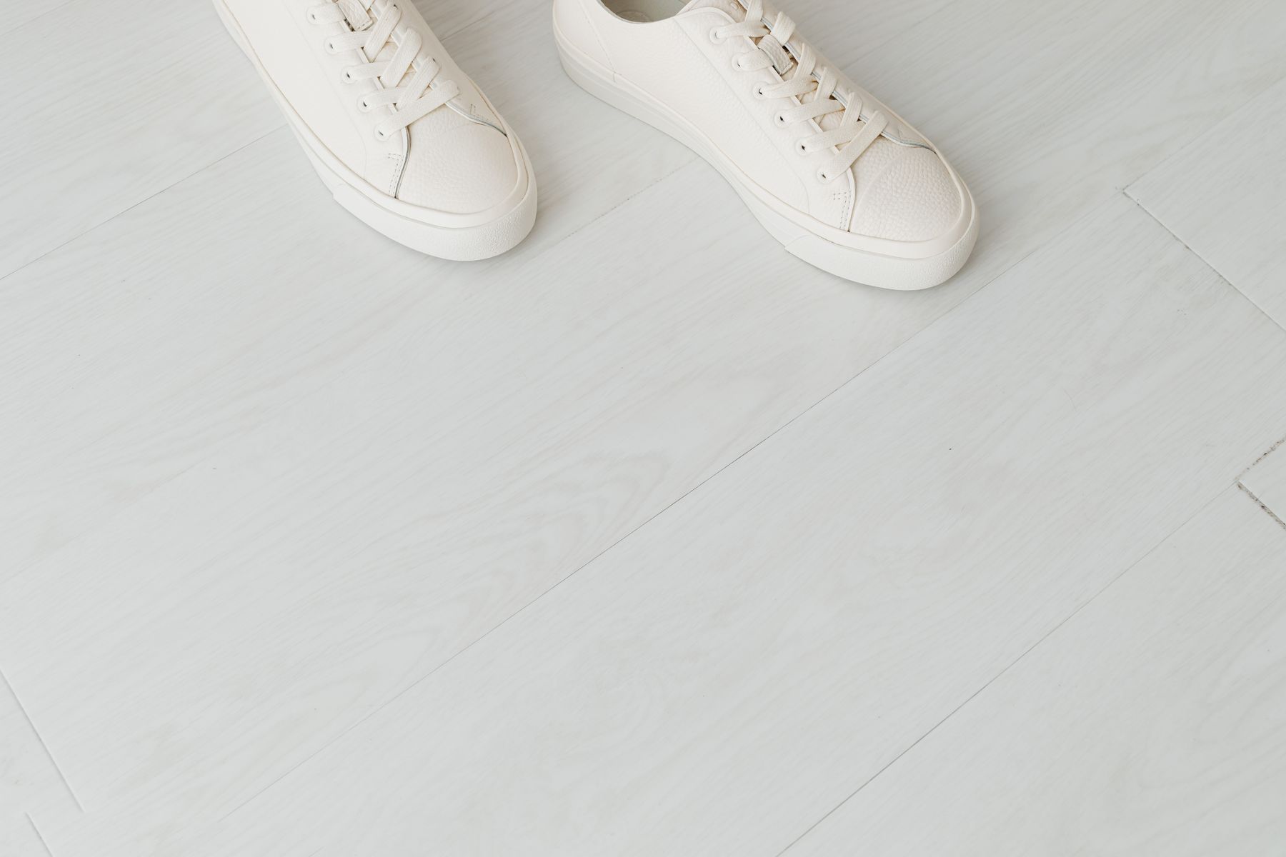 Minimal white sneakers resting on a light wood floor
