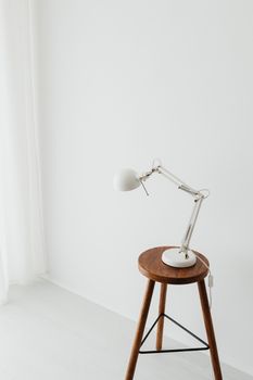 Stylish minimalist desk lamp on a wooden stool in a bright white room.