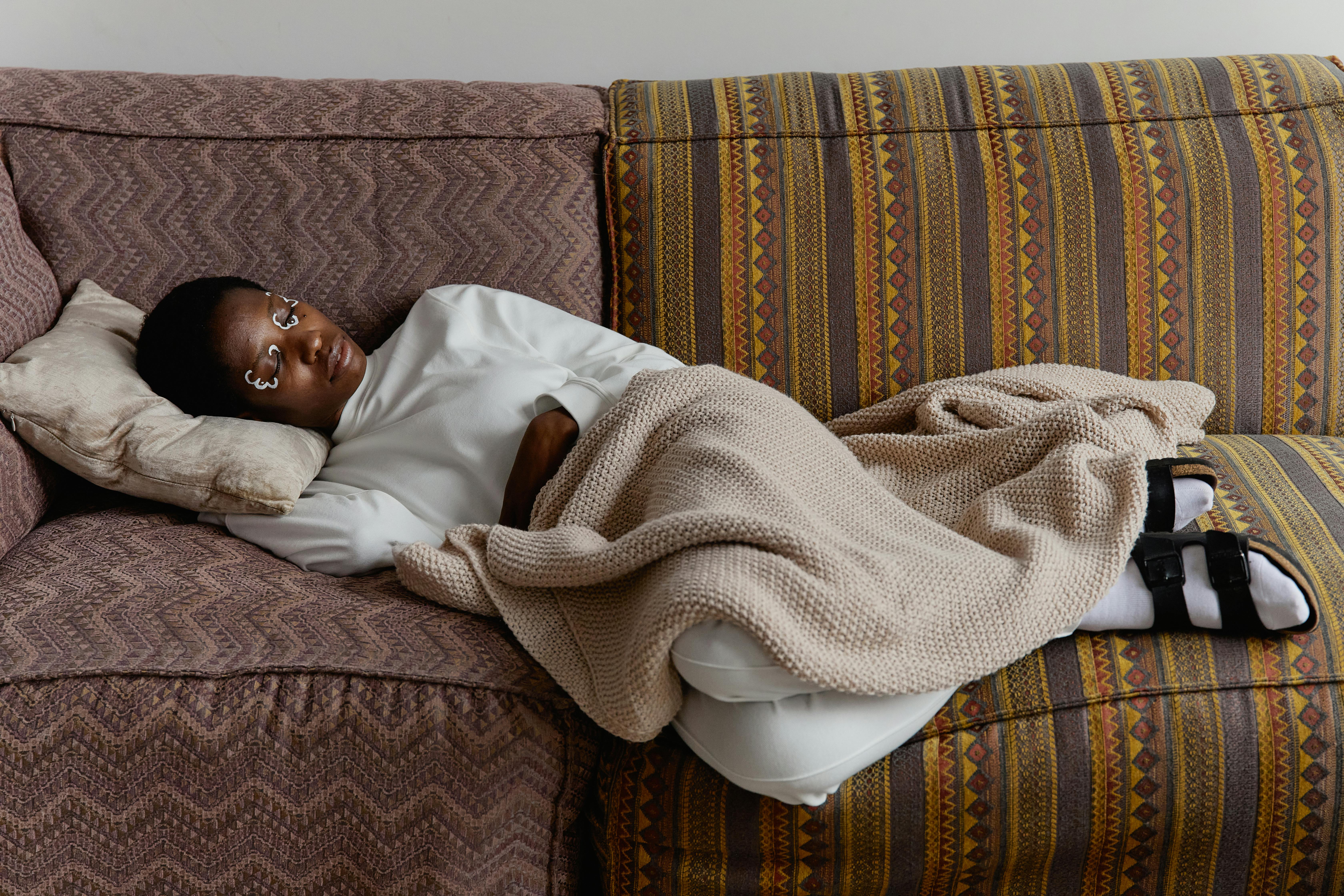 Fashionable young woman with face paint relaxing indoors on a cozy couch with blankets.