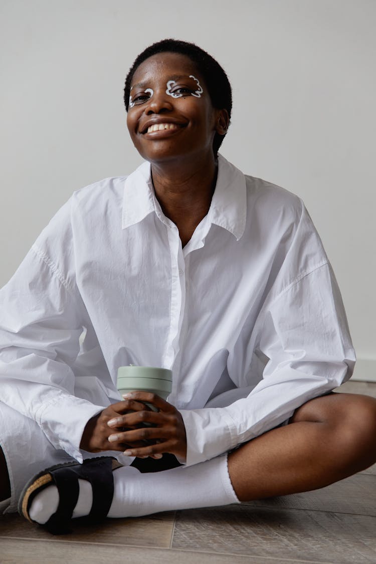 Woman In White Long Sleeves Sitting On The Floor Holding A Tumbler