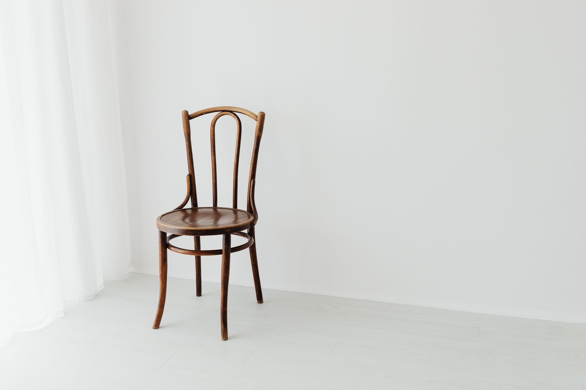 A simple wooden chair sits in a bright, minimalist interior with a white background.