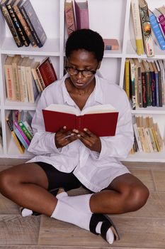 A woman sitting on the floor reading a book in a library, showcasing casual fashion and a serene indoor setting.