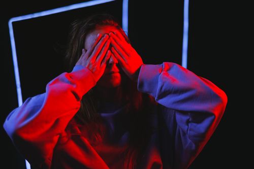 Free Moody artistic portrait of a woman with hands over face illuminated by red light. Stock Photo