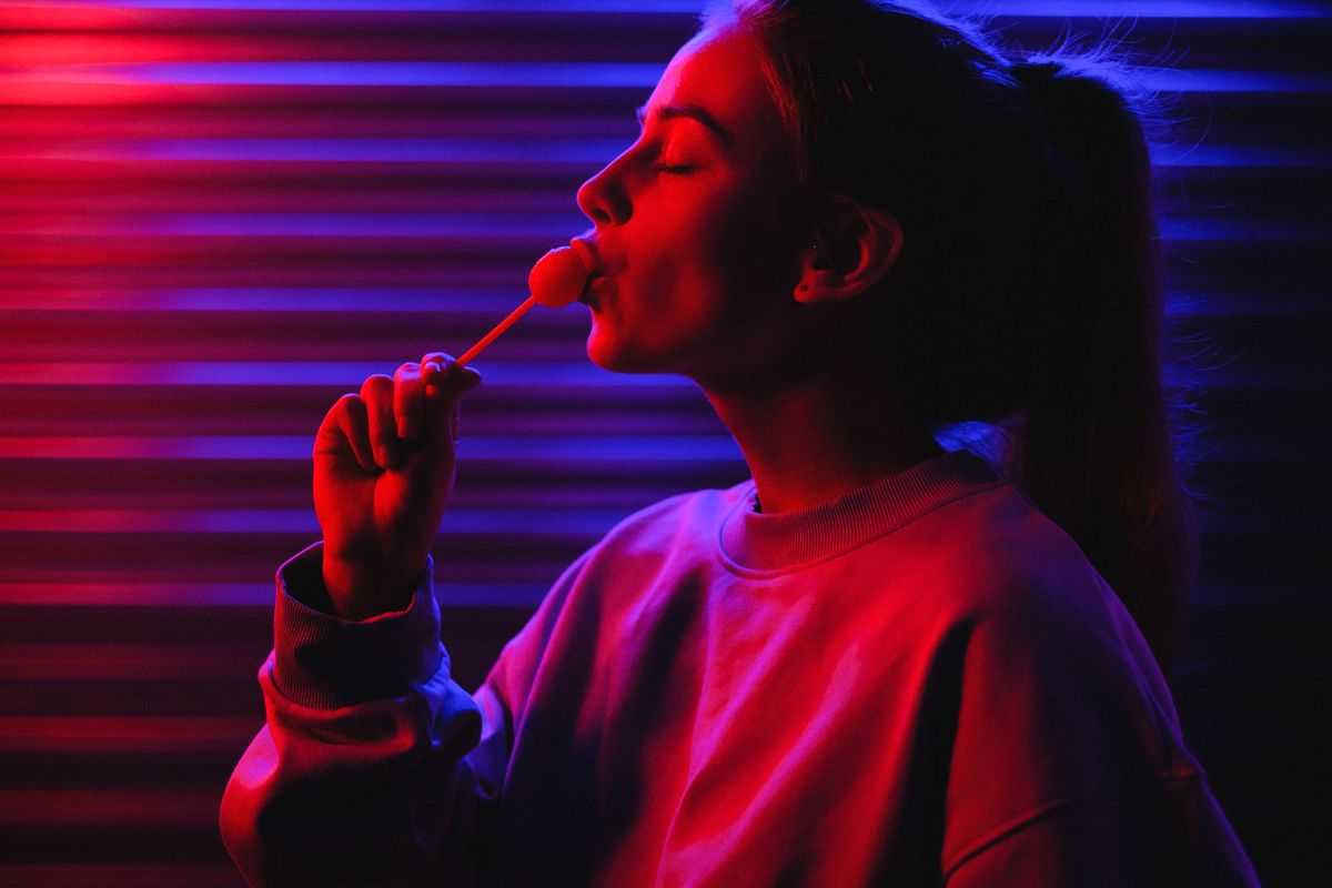 Portrait of a woman savoring a lollipop with dramatic red and blue neon lighting.