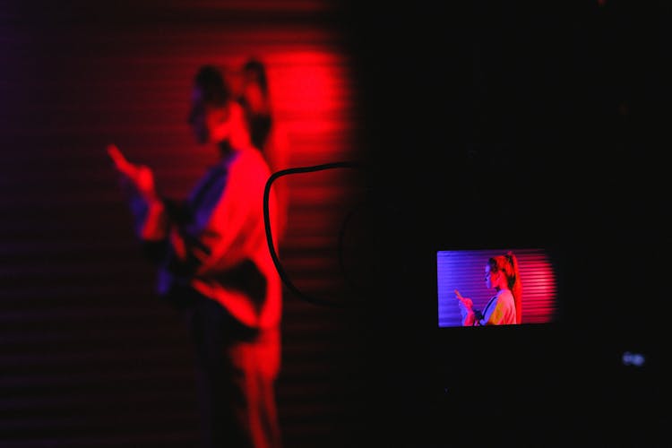 Pensive Female Browsing Smartphone While Recording Video On Camera In Dark Room