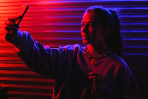 Woman in Sweater Taking Selfie while Holding Lollipop