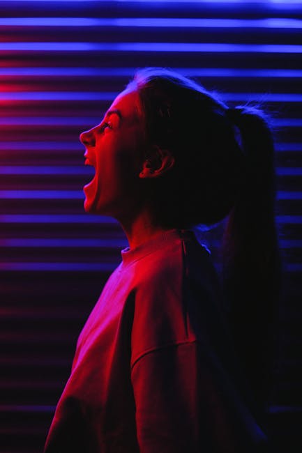 Side view of young woman in casual clothes standing and screaming in dark room with neon illumination