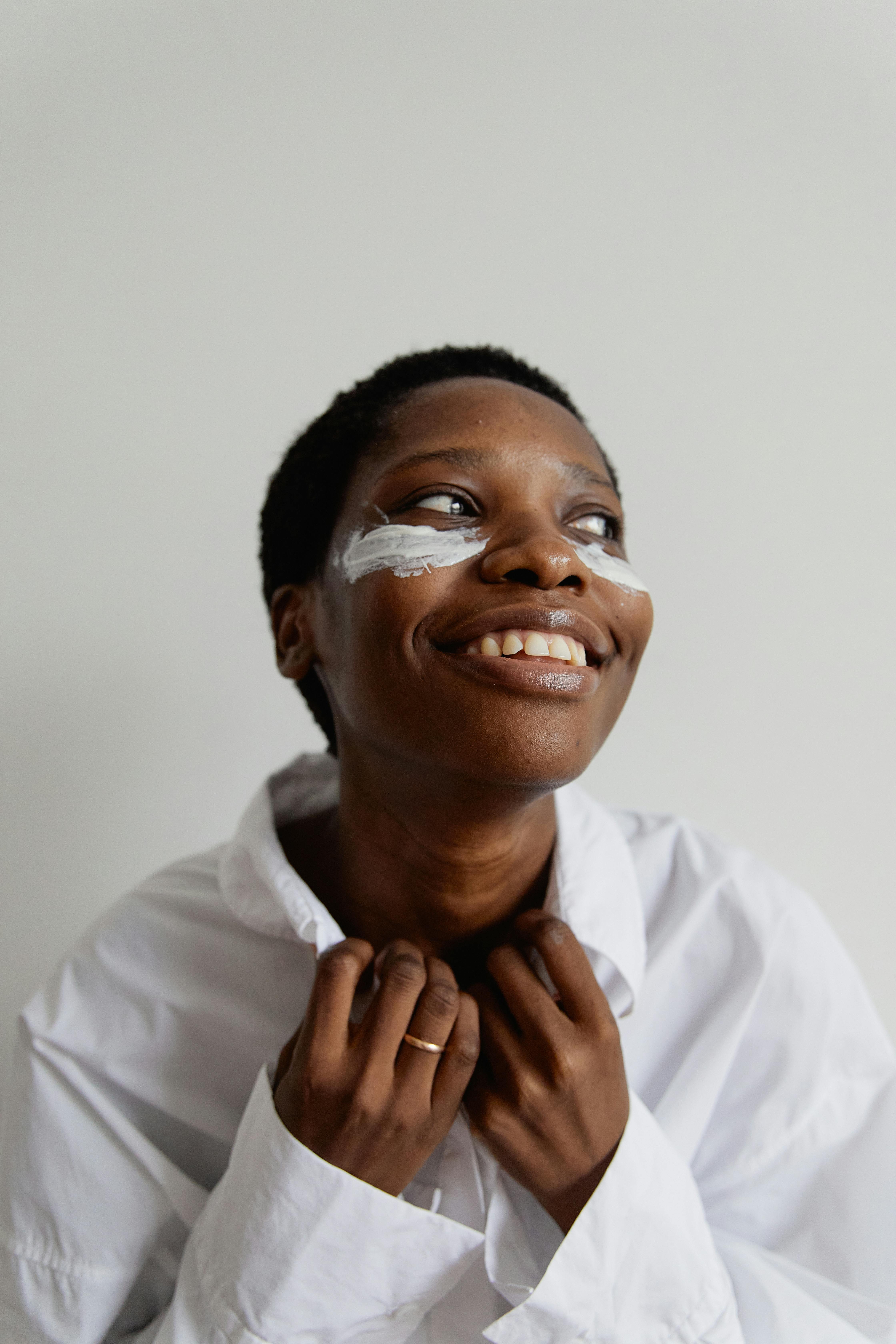 A joyful African American woman adorned with face paint, wearing a white shirt and smiling warmly.