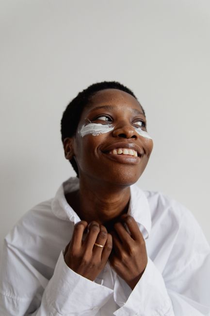 A joyful African American woman adorned with face paint, wearing a white shirt and smiling warmly.