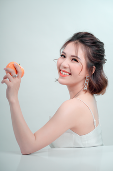 Portrait of a woman smiling while holding a peach against a white background in a studio setting.
